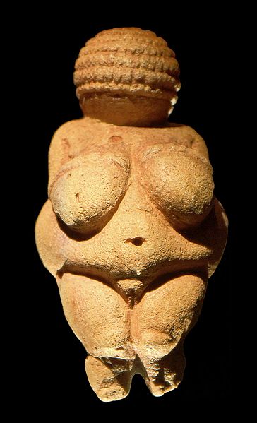 Pequeña estatuilla de piedra con forma de mujer. No tiene pies ni rostro, sus caderas y pechos están exagerados.