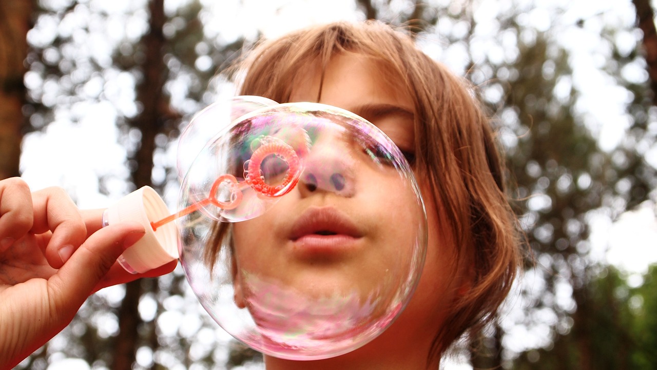 Primer plano con rostro de niña haciendo burbujas de jabón