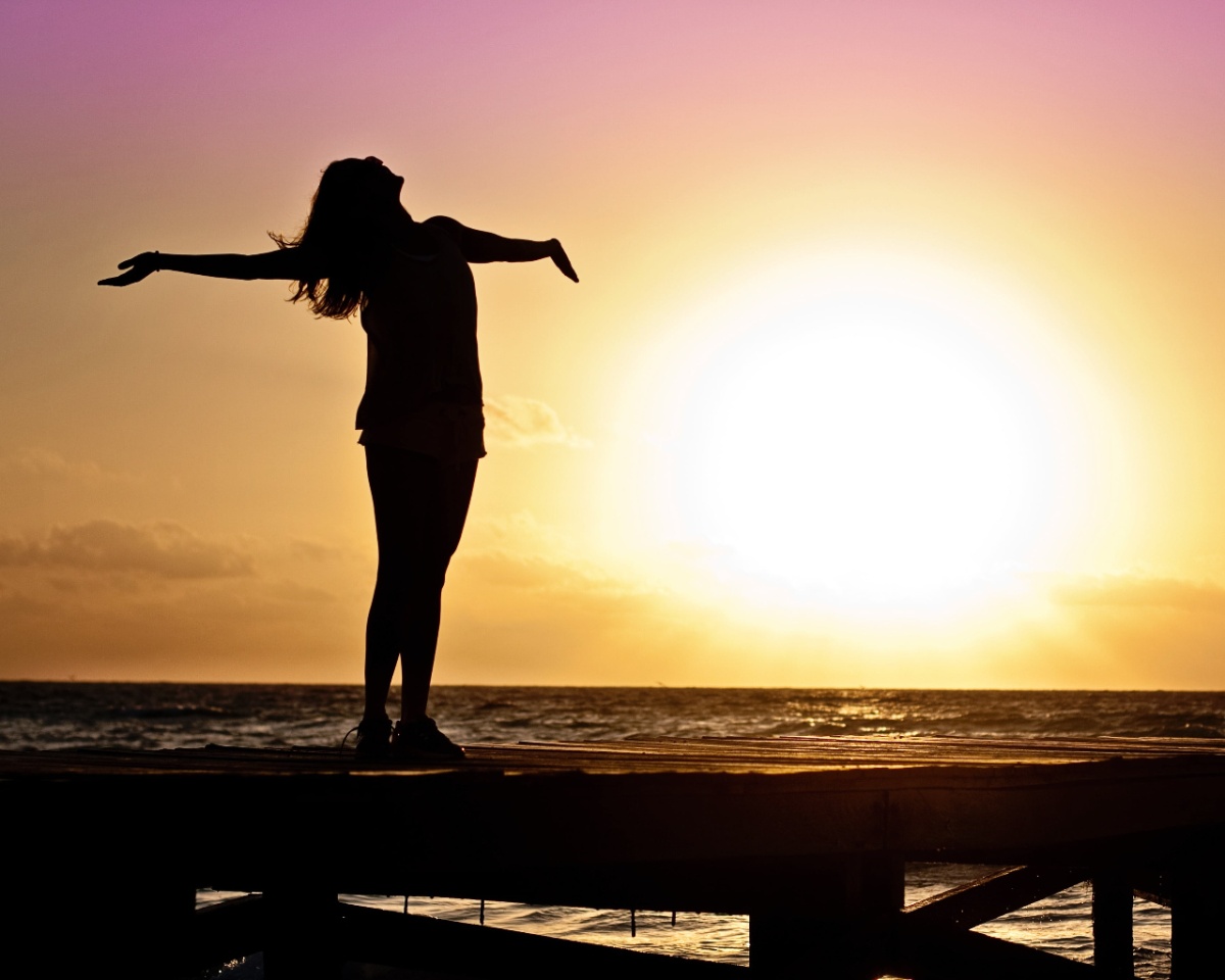 mujer con sus brazos extendidos, sobre un muelle,con atardecer de fondo