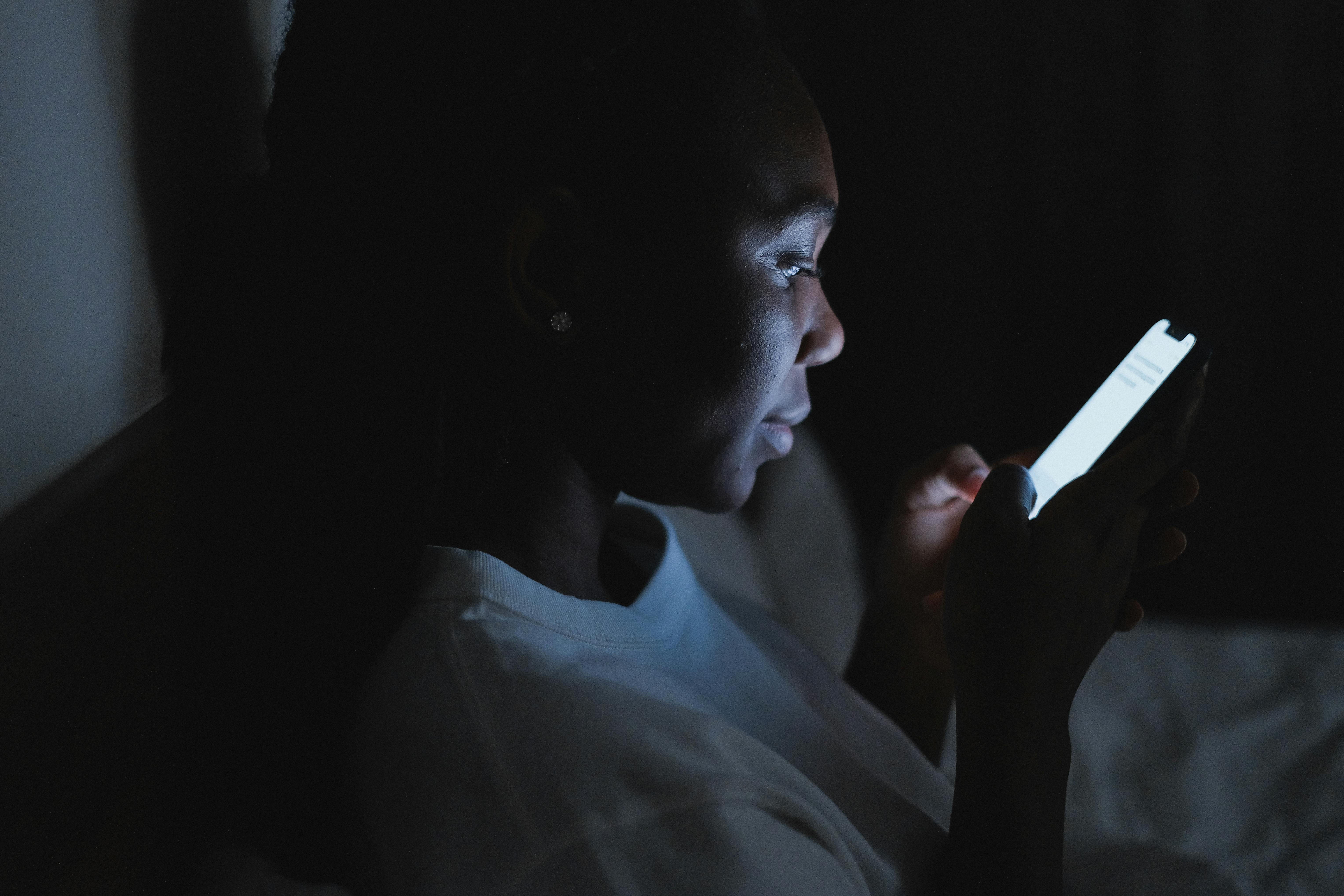 Persona en la noche observando una pantalla de celular. Edad indeterminada, puede ser adolescente o adulto joven.