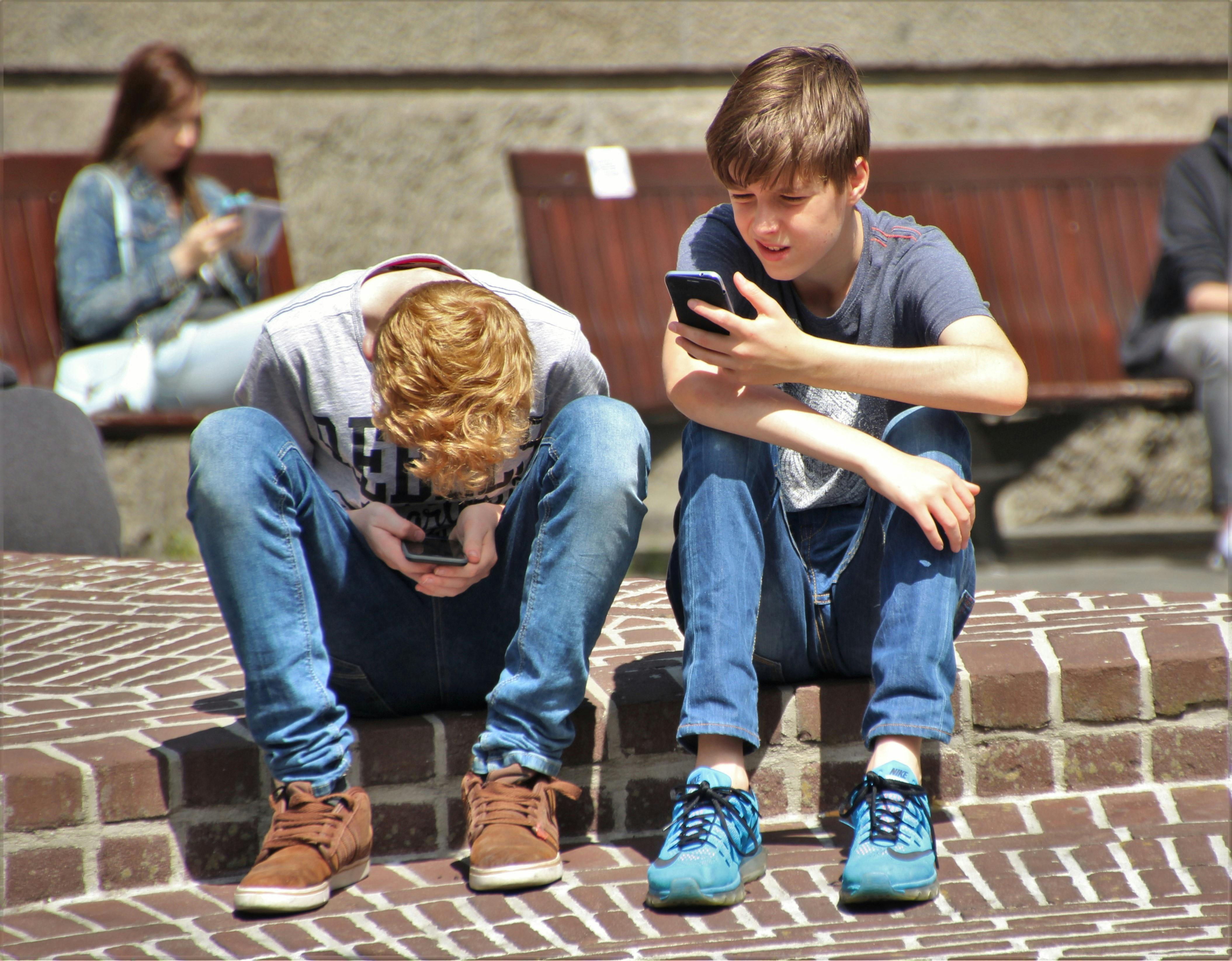 Dos adoelscentes en un patio escolar mirando sus dispositivos móviles