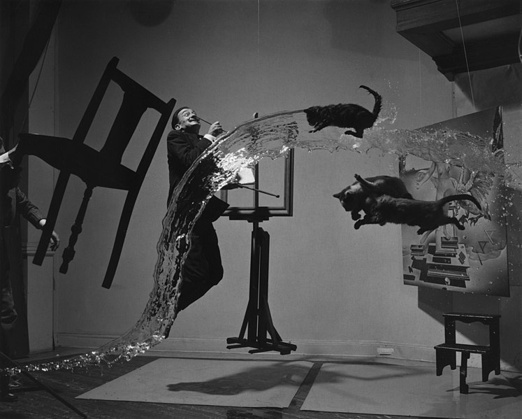 Fotografía surrealista en la que se yuxtaponen imágenes incongruentes. Un par de gatos vuelan en el aire, un hombre salta frente a un espejo, las sillas flotan y el agua está suspendida en el aire.
